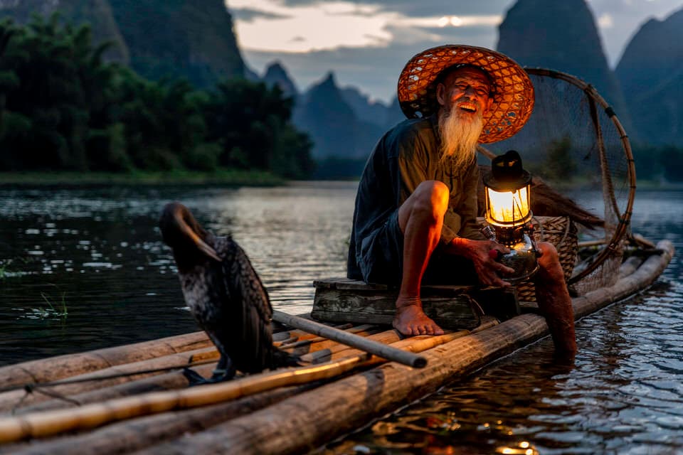 Cormorant fisherman on a bamboo raft with a lantern at sunset in Guilin, China.