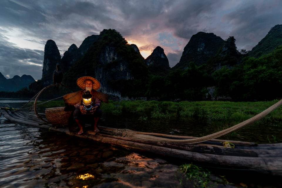 A cormorant fisherman lighting his lantern on a bamboo raft in Guilin at sunset.