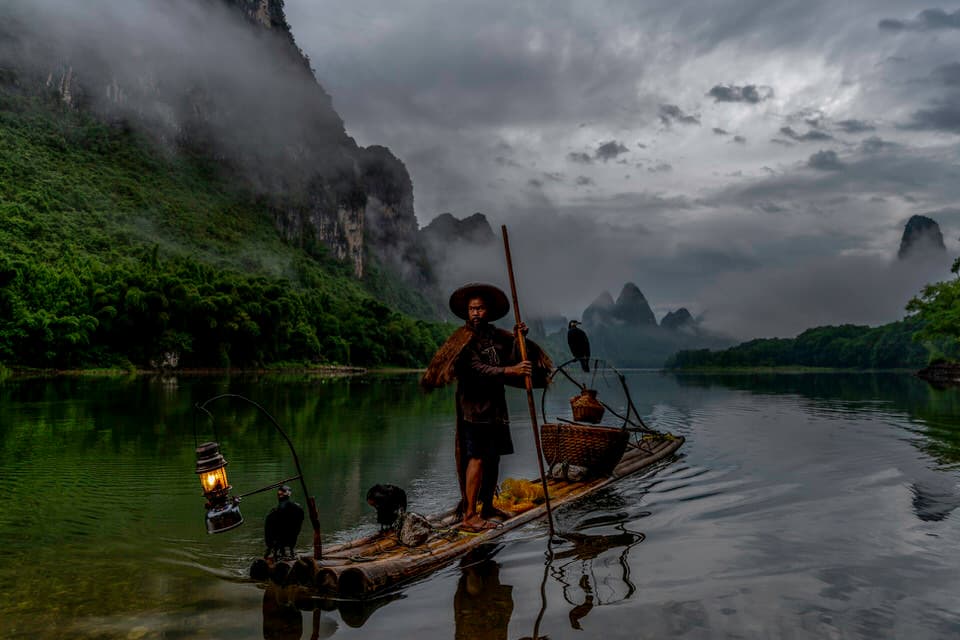 A cormorant fisherman with his bird at sunrise on the Li River in Guilin, China.