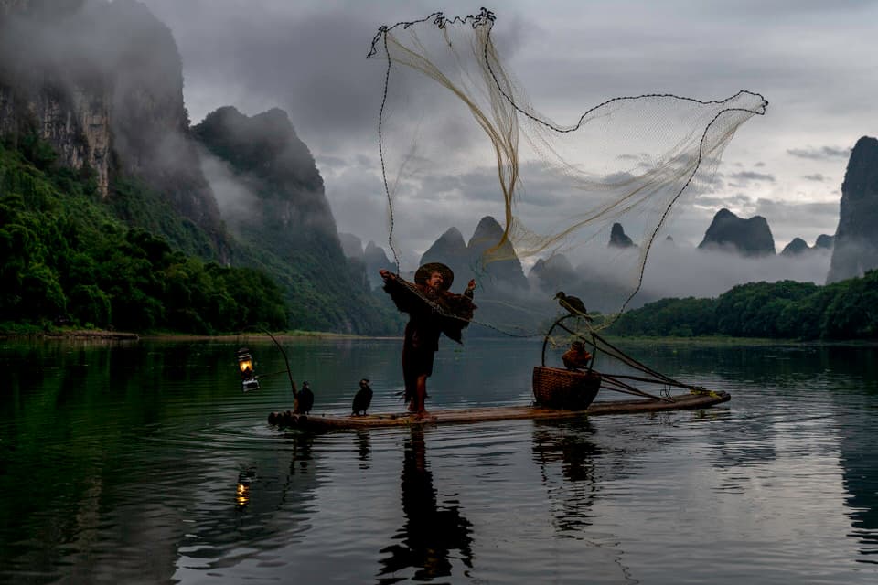 Cormorant fisherman casting his fishing net at sunrise on the Li River in Guilin, China.