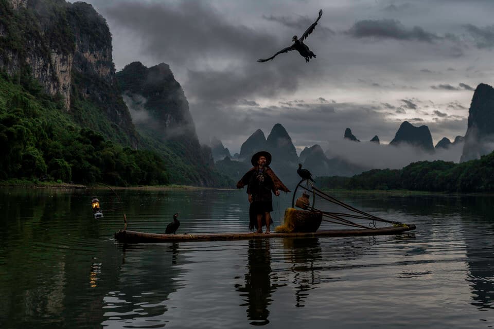 A cormorant fisherman with a bird flying at sunrise on the Li River in Guilin, China.