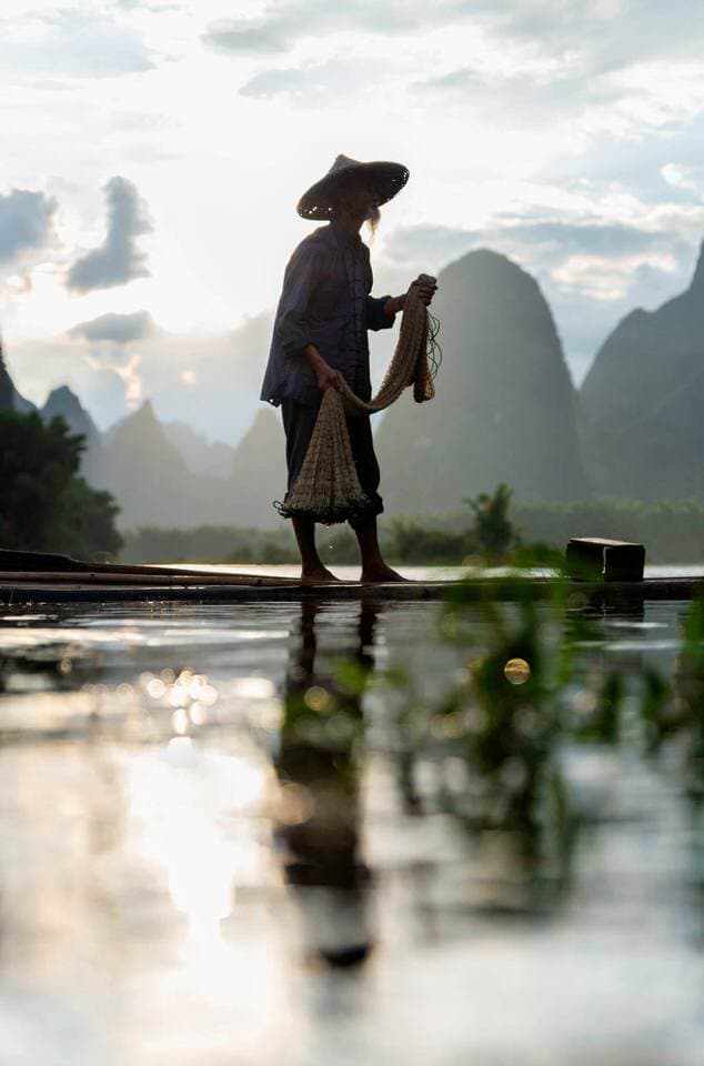 Cormorant fisherman standing on a bamboo raft in the Li River preparing to cast his net at sunrise in Guilin, China.