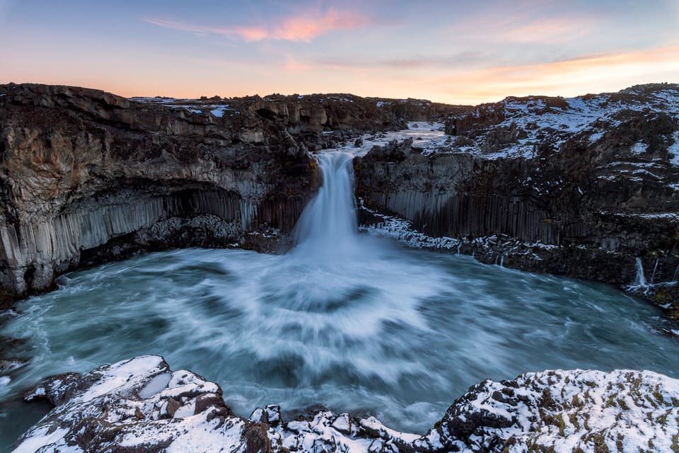 Aldeyjarfoss waterfall flowing in Iceland surrounded by basalt rock formations and snow at sunrise