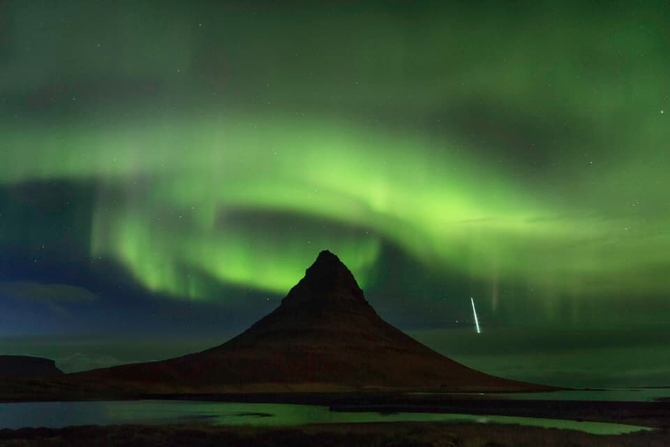 Northern Lights over a mountain in Iceland with a shooting star in the night sky