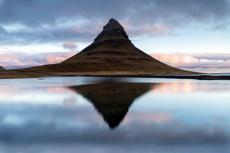 Kirkjufell mountain reflected in still lake water under dramatic clouds in Iceland