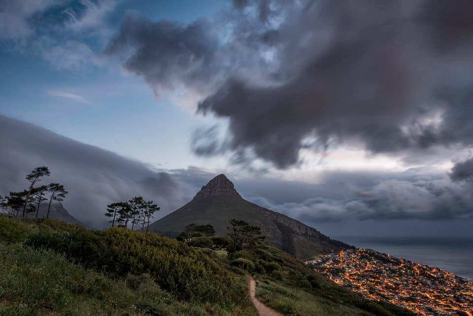 Lions Head mountain with Cape Town city lights under dramatic clouds at dusk