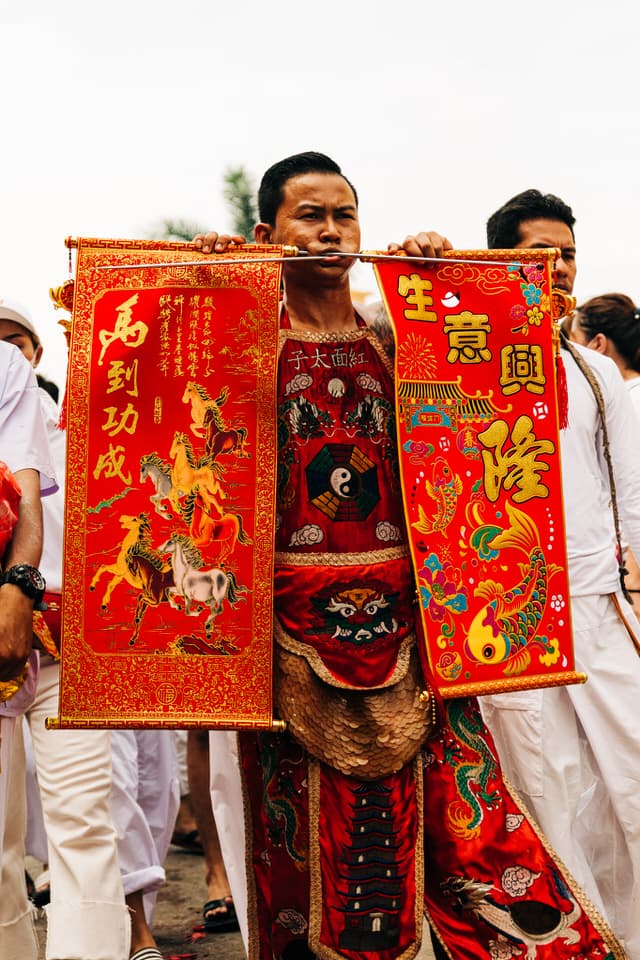 Devotee with cheek piercings holding banners during Phuket Vegetarian Festival.