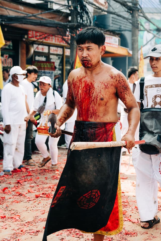 Devotee with ceremonial weapons and bloodstained torso at Phuket Vegetarian Festival.