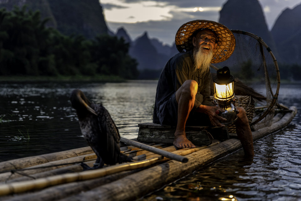 Traditional cormorant fishermen using ancient fishing techniques on Chinese river - cultural heritage photography documenting traditional fishing methods